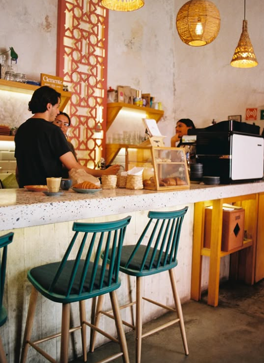 Interior de Clemente con barra de terrazo y sillas de madera, luz de día